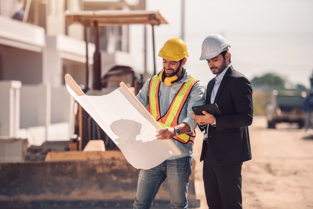 civil-engineer-construction-worker-manager-holding-digital-tablet-blueprints-talking-planing-about-construction-site-cooperation-teamwork-concept-min